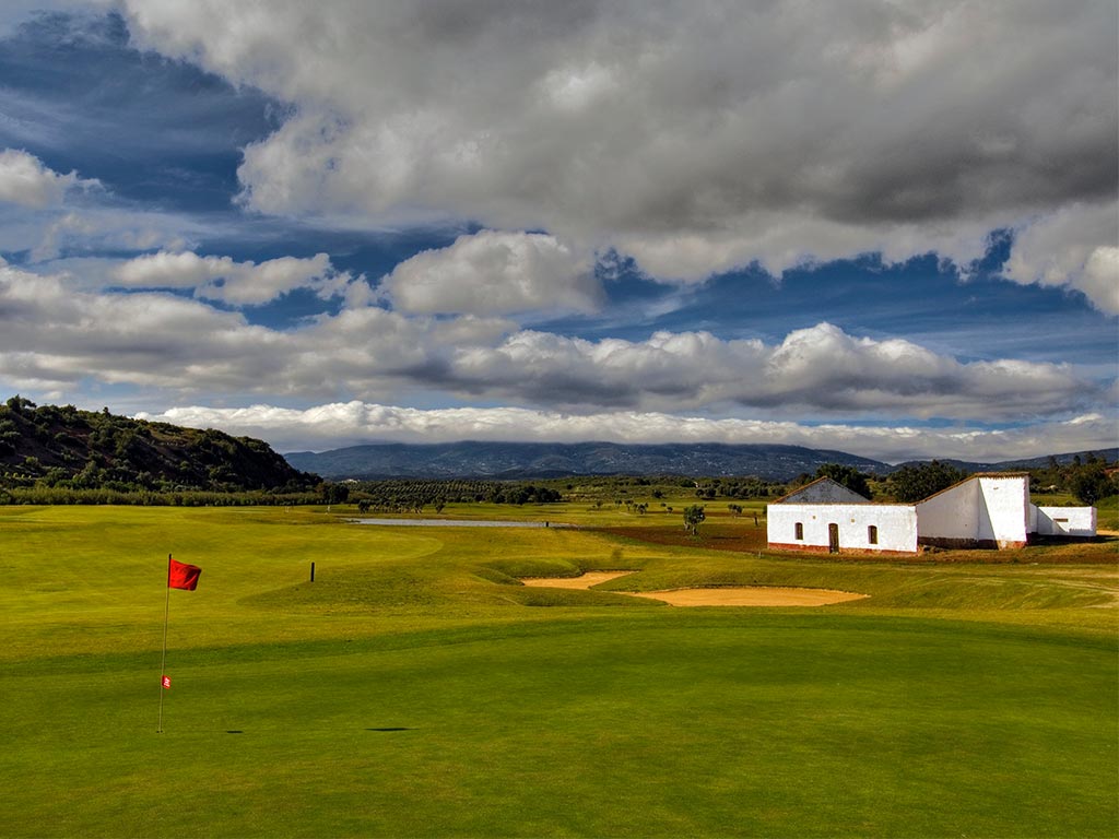 Ciel nuageux, bâtiment et drapeau sur le green du Morgado Golf Course